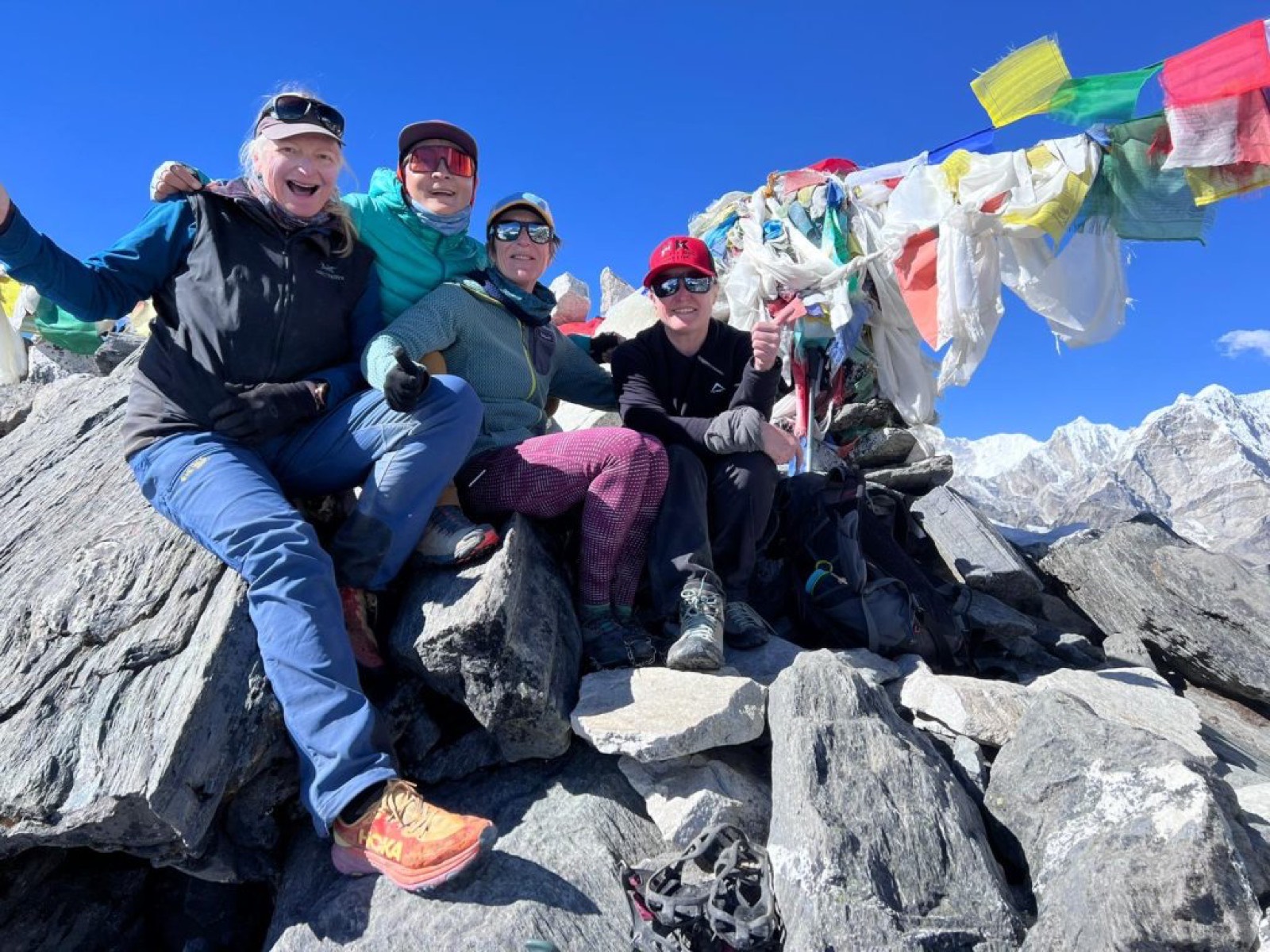 Four trekkers celebrating on a rocky pass under prayer flags in the Khumbu