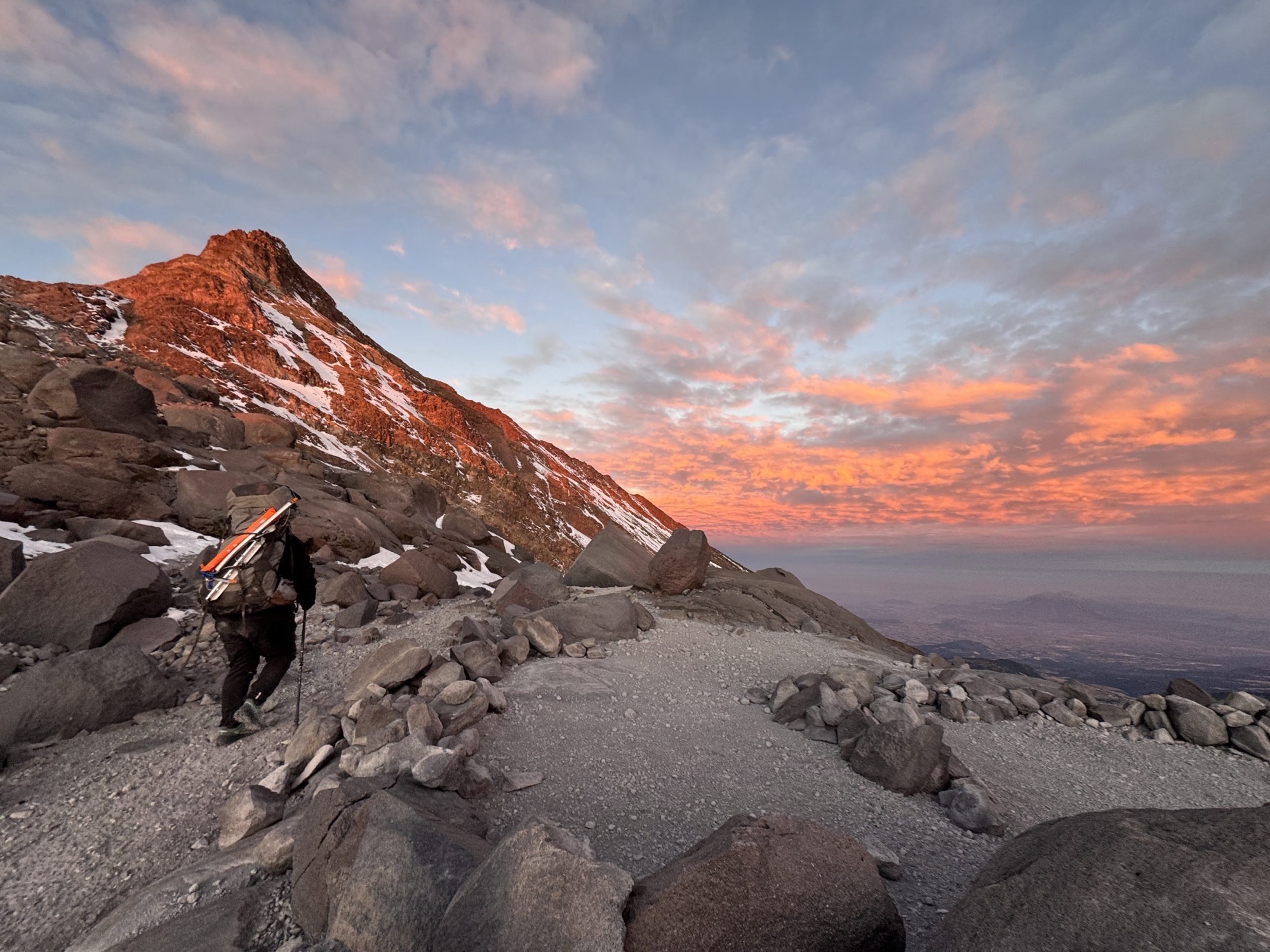 A climber with a heavy pack on the rocky slopes of Pico de Orizaba at sunrise
