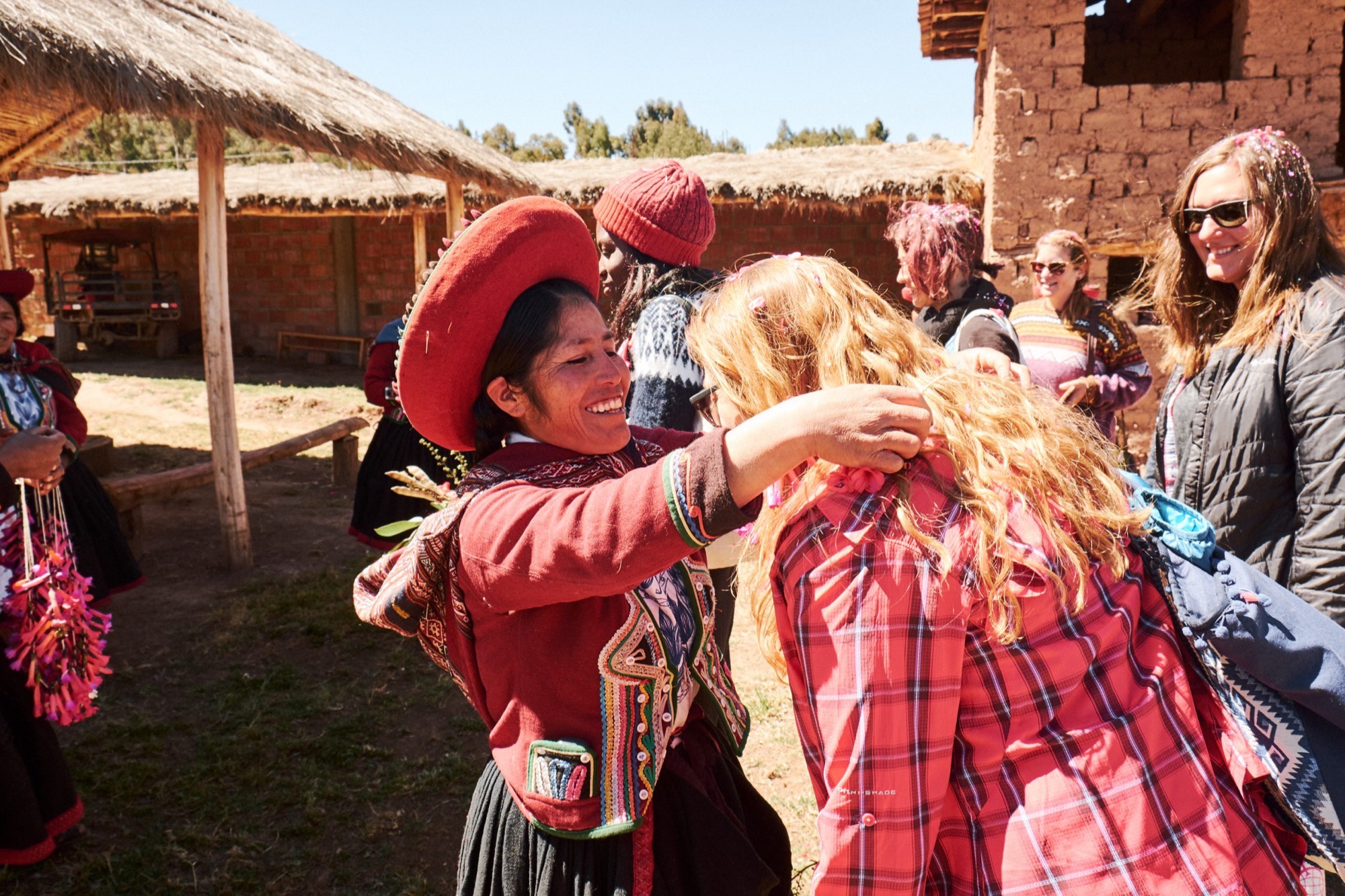 A woman in a red Peruvian hat hugging a trekker in a village